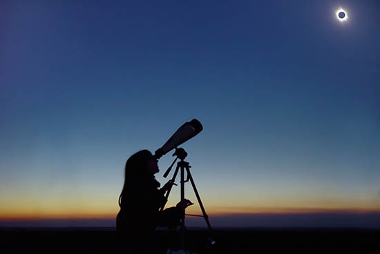 Girl looking through a telescope at a solar eclipse